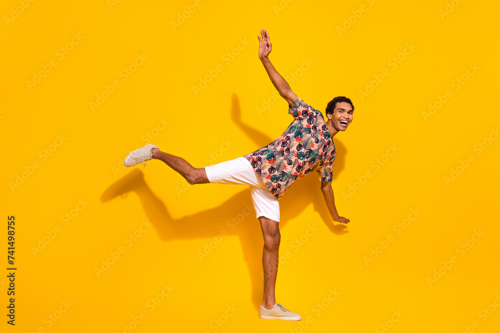 Full length body photo of funky young positive student guy standing one leg trying stay balanced isolated on yellow color background