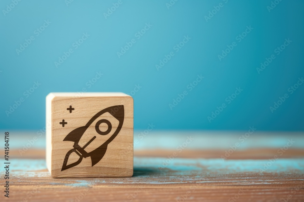 Wooden block with rocket printed on it, startup and business concept, blue background. Wooden block with rocket printed on it, startup and business concept, blue background.