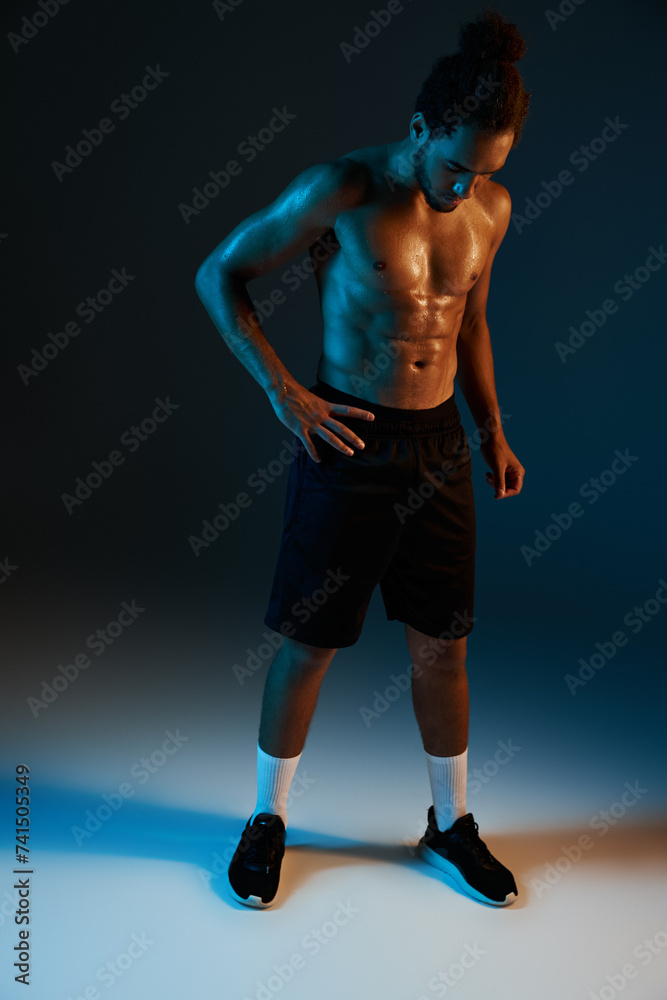 young shirtless african american man in black shorts posing in gym on dark lighted background young shirtless african american man in black shorts posing in gym on dark lighted background