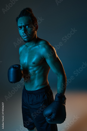 appealing young african american man in black shorts with boxing gloves looking at camera in gym