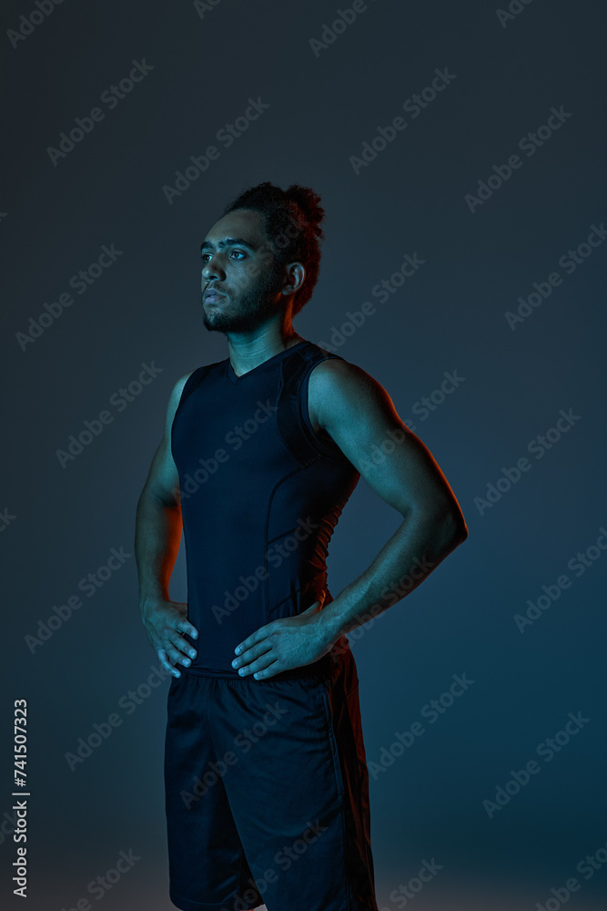 sporty african american man in comfy sportwear posing with arms akimbo on dark lighted background