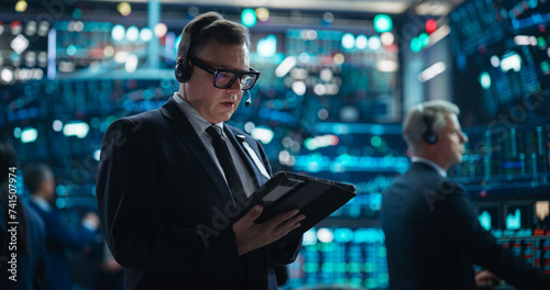 Portrait of a Successful Stock Exchange Manager Working in a Modern Office. Professional Trader Browsing Internet on a Tablet Computer, Using Software with Online Stock Market Data Prediction
