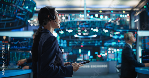 Young Asian Female Broker Working on Tablet Computer on Stock Exchange Floor. Traders Monitoring Real-Time Stocks, Commodities and Exchange Market Data. Professional Investment Agents in Office