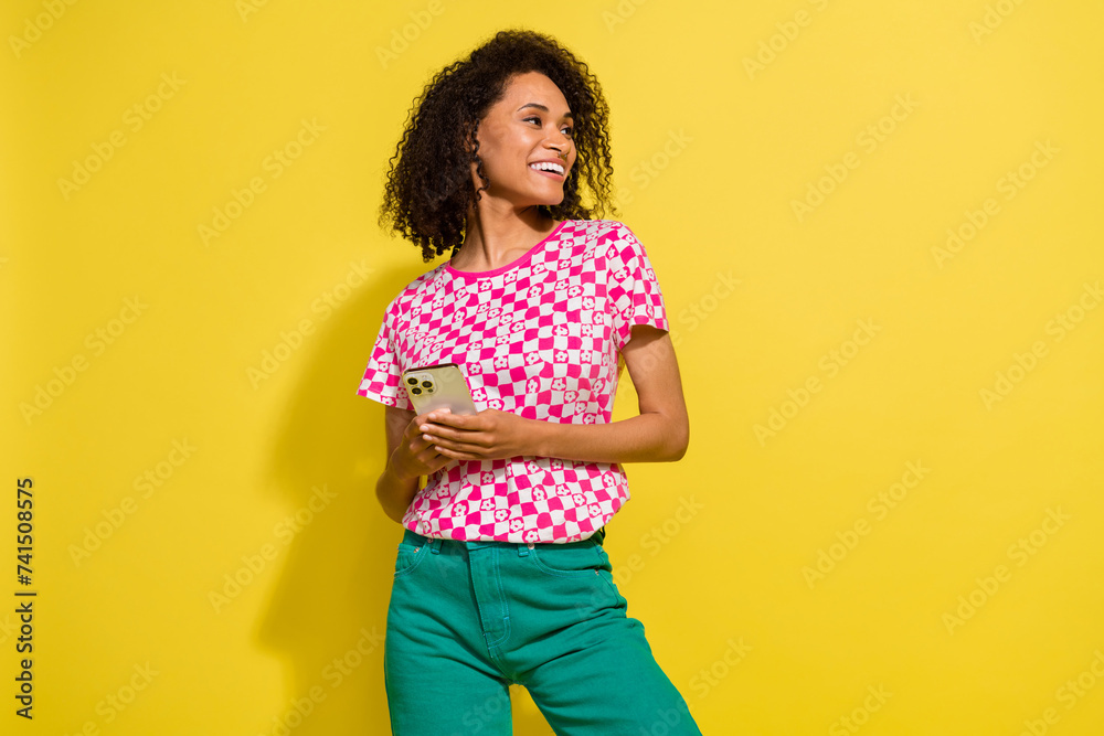 Portrait of charming creative person hold smart phone look empty space isolated on yellow color background Portrait of charming creative person hold smart phone look empty space isolated on yellow color background