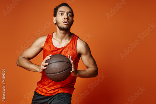 attractive athletic african american man in sportwear playing basketball actively on orange backdrop © LIGHTFIELD STUDIOS