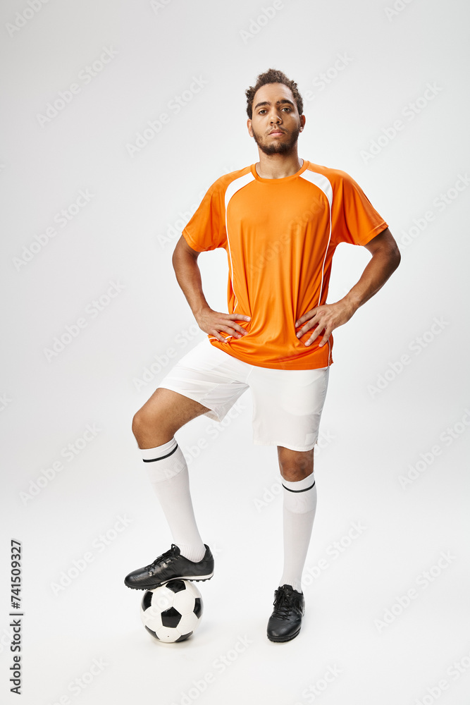 Obraz premium handsome african american man in sportwear with football with arms akimbo and looking at camera