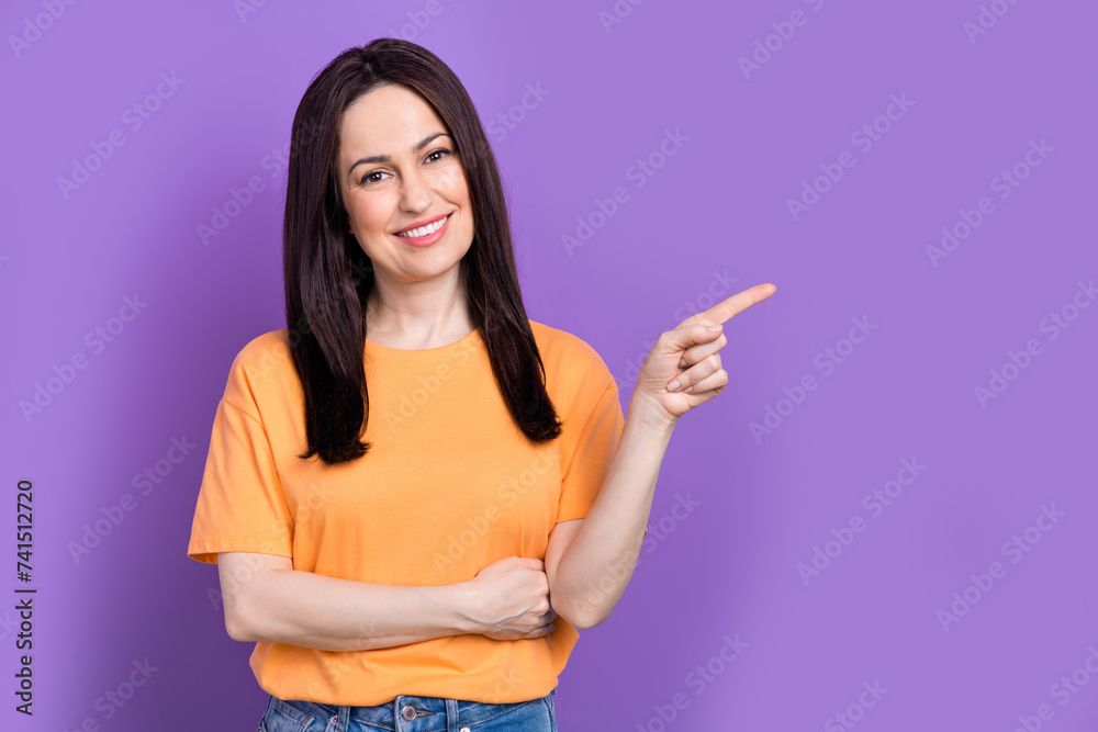 Portrait of brunette model young woman in yellow t shirt directing finger empty space shopping there isolated on purple color background Portrait of brunette model young woman in yellow t shirt directing finger empty space shopping there isolated on purple color background