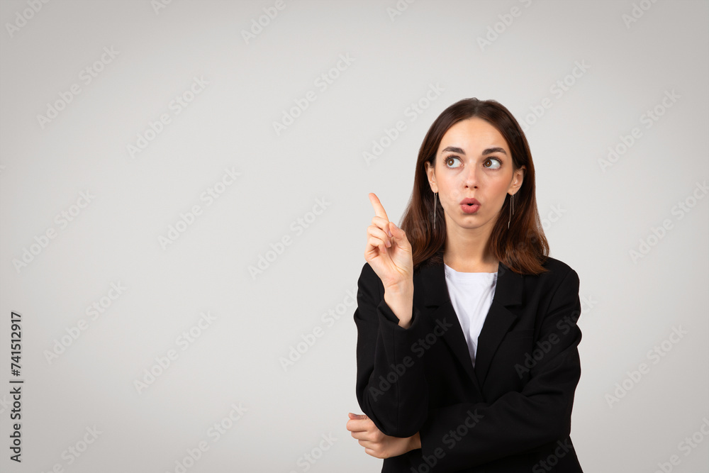 Surprised businesswoman with wide eyes pointing upwards, having an idea or realization Surprised businesswoman with wide eyes pointing upwards, having an idea or realization