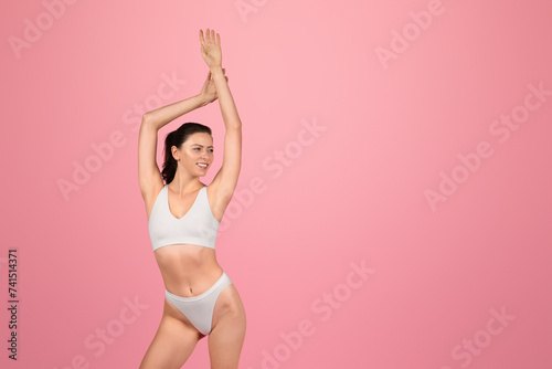 Active young woman in white sportswear stretches with arms raised, showcasing a fitness © Prostock-studio