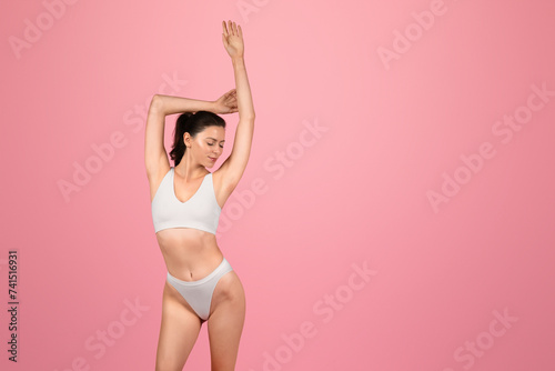A serene woman in a white sports bra and underwear stretches her arms above her head © Prostock-studio