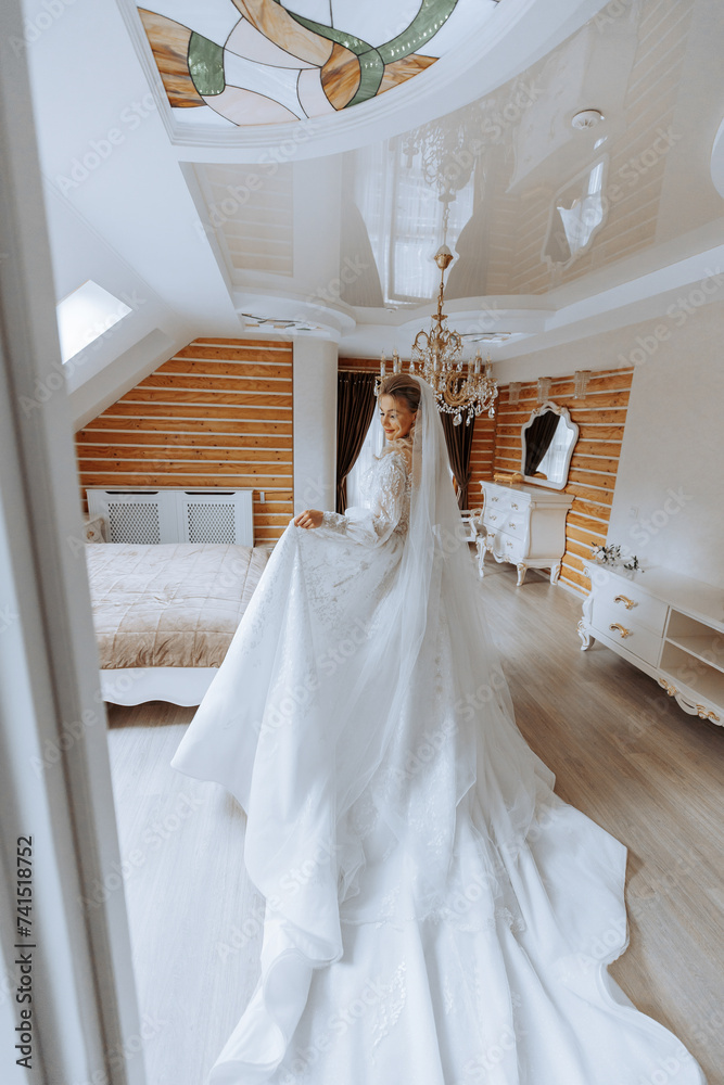 Young brunette in long wedding dress and veil in hotel room. A charming bride, full length, in a magnificent white dress on the morning before the wedding.