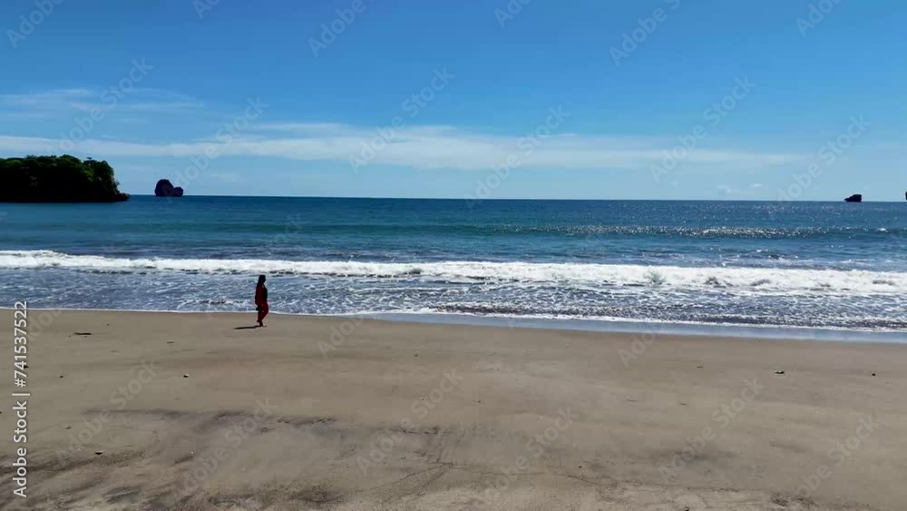 Aerial view from behind of a woman walking along the waterfront of a pristine beach with turquoise waters on a tropical island Aerial view from behind of a woman walking along the waterfront of a pristine beach with turquoise waters on a tropical island