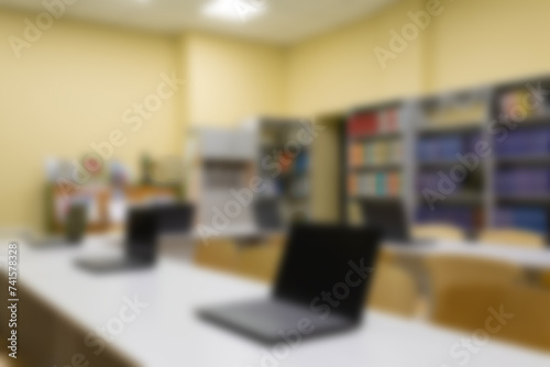 Blurred photo of an empty school library with laptops on tables. Abstract light bokeh on the background of a school interior for design