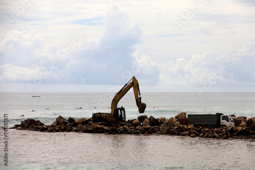 Trucks and excavators are working to unload material for a reclamation project on the coast of Bali, Indonesia. the process of making embankments on the beach to anticipate abrasion.
