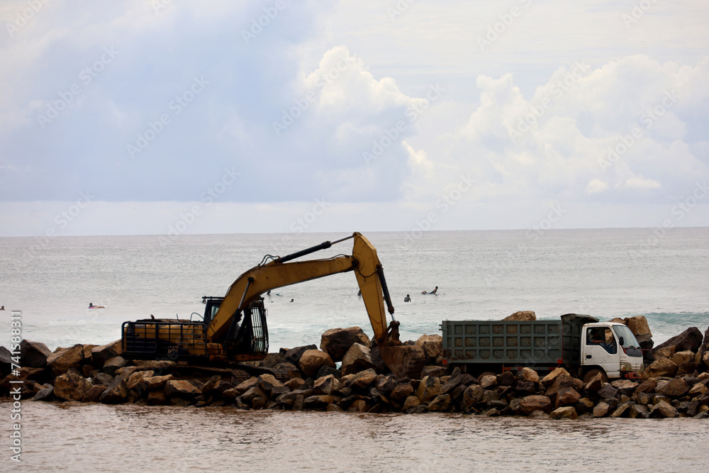Trucks and excavators are working to unload material for a reclamation project on the coast of Bali, Indonesia. the process of making embankments on the beach to anticipate abrasion.