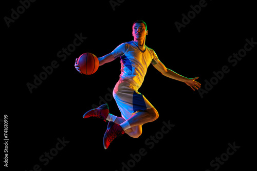 Sportsman, basketball player in motion about to make accurate pass against black studio background in mixed neon light. Concept of professional sport, energy, match, championship, tournament.