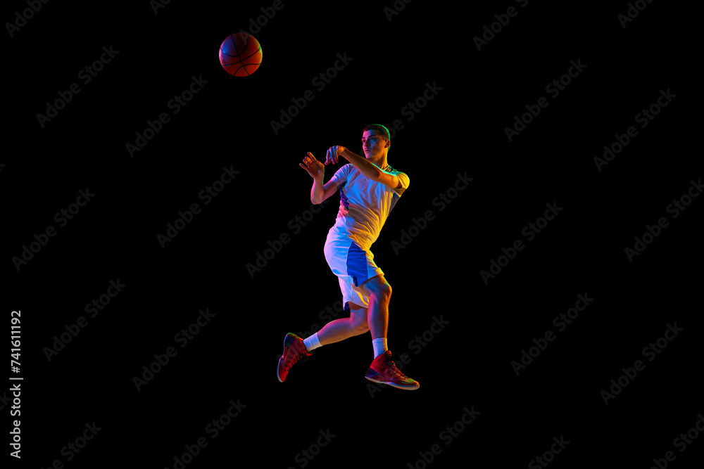 Body size photo of young athlete man doing powerful pass in action against black studio background in mixed neon light. Concept of professional sport, energy, strength and power, match, tournament.