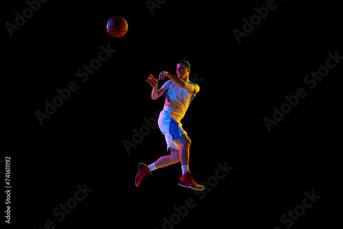 Body size photo of young athlete man doing powerful pass in action against black studio background in mixed neon light. Concept of professional sport, energy, strength and power, match, tournament.