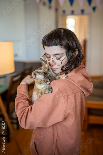 Caring pet owner tenderly hugs cute Devon Rex cat supporting each other. Kind young woman affectionately holds stray cat has found new home. Warm friendly embrace between domestic animal and teen girl