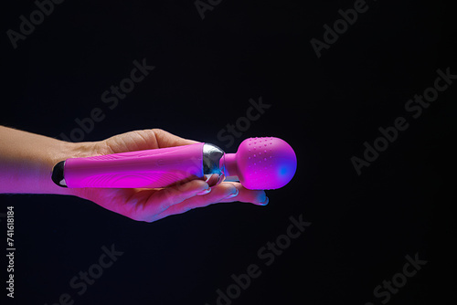 The girl is holding a sex shop toy. Sex toy clitoral vibrator on a black background with neon lights.