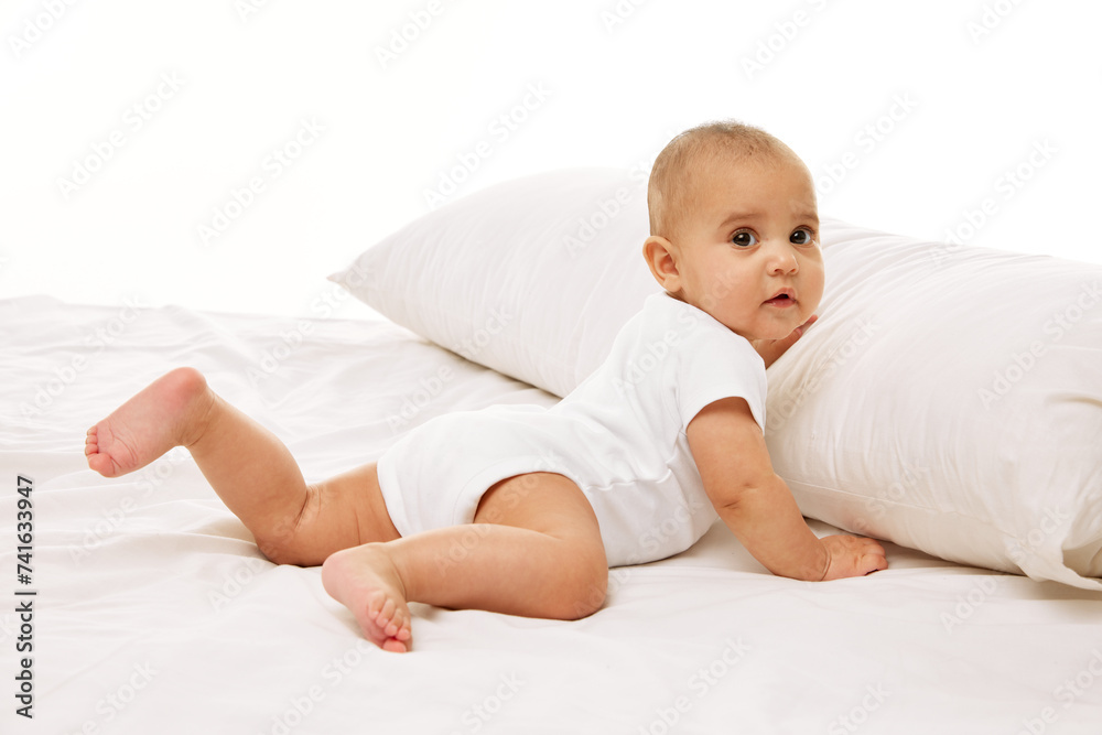 Portrait of beautiful little baby girl, toddler in onesie posing on bed against white background. Healthcare and education. Concept of childhood, family, care, motherhood, infancy, heath Portrait of beautiful little baby girl, toddler in onesie posing on bed against white background. Healthcare and education. Concept of childhood, family, care, motherhood, infancy, heath