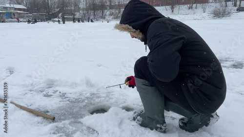 Winter ice fishing. A fishingman holds a fishing rod near a hole in the ice. The man was fishing in the fresh air. A boy's winter hobby. High quality 4k footage. High quality 4k footage photo