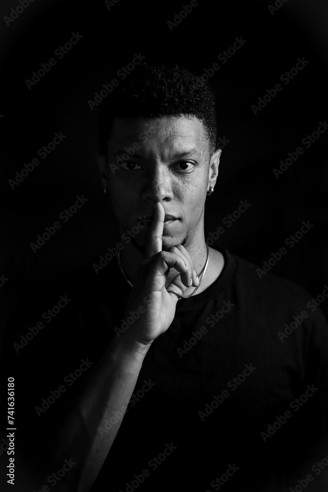 Serious young man making silence gesture. black and white photography