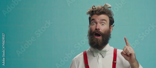 Emotional bearded male has surprised facial expression astonished look dressed in white shirt with red braces points with index finger at upper right corner shows copy space for advertisement photo