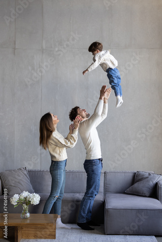 Family, father lifting child on sofa at home. Dad playing flying plane in air game with son on living room couch
