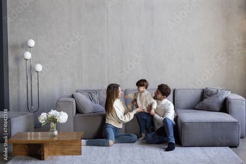 Portrait of excited young parents with cute little son posing in new apartment