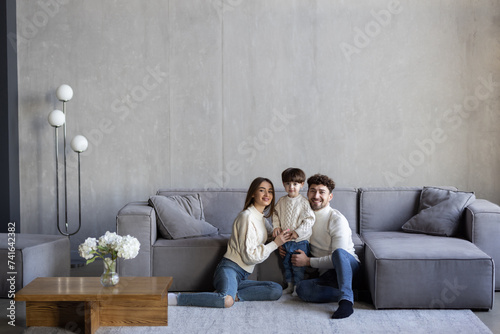 Portrait of happy young Caucasian family with little boy son sit on sofa in new own cozy home.