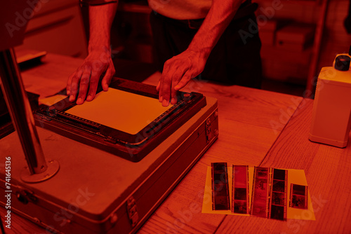 cropped young man focuses on delicate process of enlarging film in darkroom with red light photo