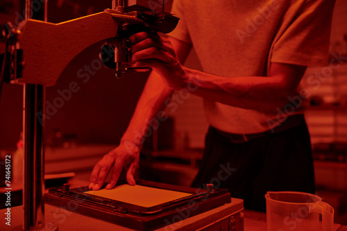 cropped photographer focuses on delicate process of enlarging film in darkroom with red light photo