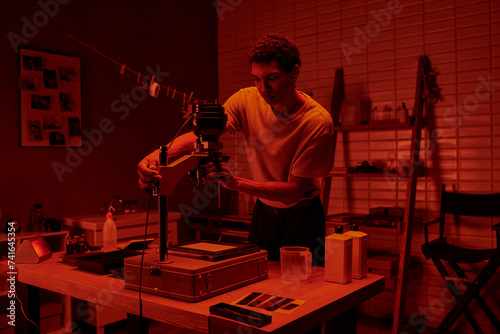 In a darkroom with red light, photographer focuses intently on delicate process of enlarging film