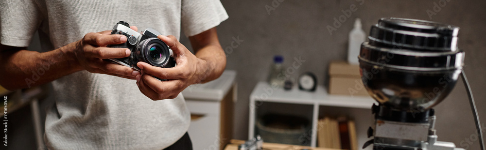 cropped black man Intently holding an analog camera while standing in a photo lab, banner