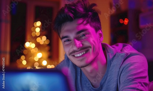 Young man cheerful smiling programmer or influencer working from cozy home using his laptop and decorated aparment with LED lights photo