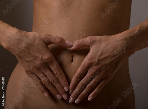 Close-up of woman's hands making a heart on her stomach