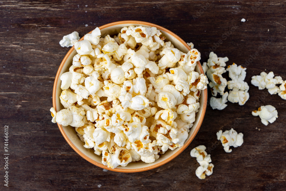 A plate of popcorn on a brown table , top view. A plate of popcorn on a brown table , top view.
