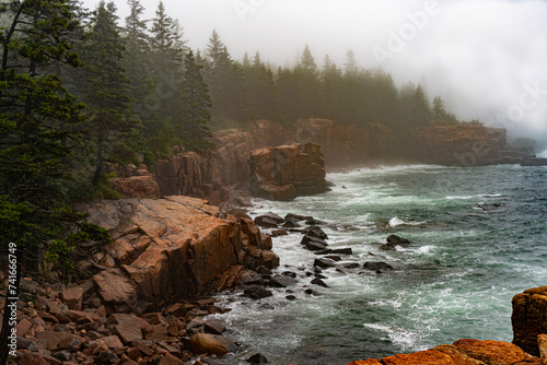 Thunder Hole, Acadia National Park, Maine. Foggy, rainy natural rock inlet where waves crash. Emerald Atlantic Ocean waves on red granite rocks, ocean cliffs. 