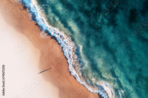 Aerial view of a white sandy beach with white waves rolling onto shore and crystal clear blue water and a girl standing on the beach casting a long shadow, Port Noarlunga, South Australia, Australia. photo