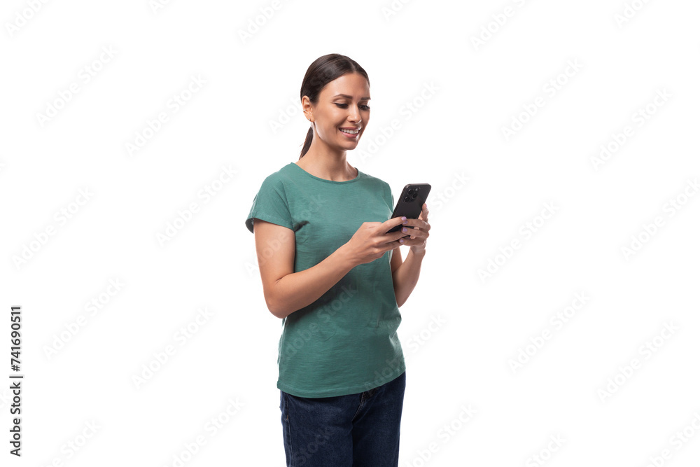 well-groomed young brunette woman dressed in a green t-shirt and jeans uses a mobile phone well-groomed young brunette woman dressed in a green t-shirt and jeans uses a mobile phone