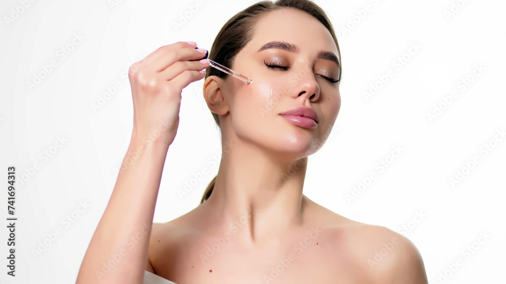 Close-up studio portrait of a young woman, isolated on a light background, applying serum from a pipette. Natural organic cosmetic product for facial skin care and skin regeneration.