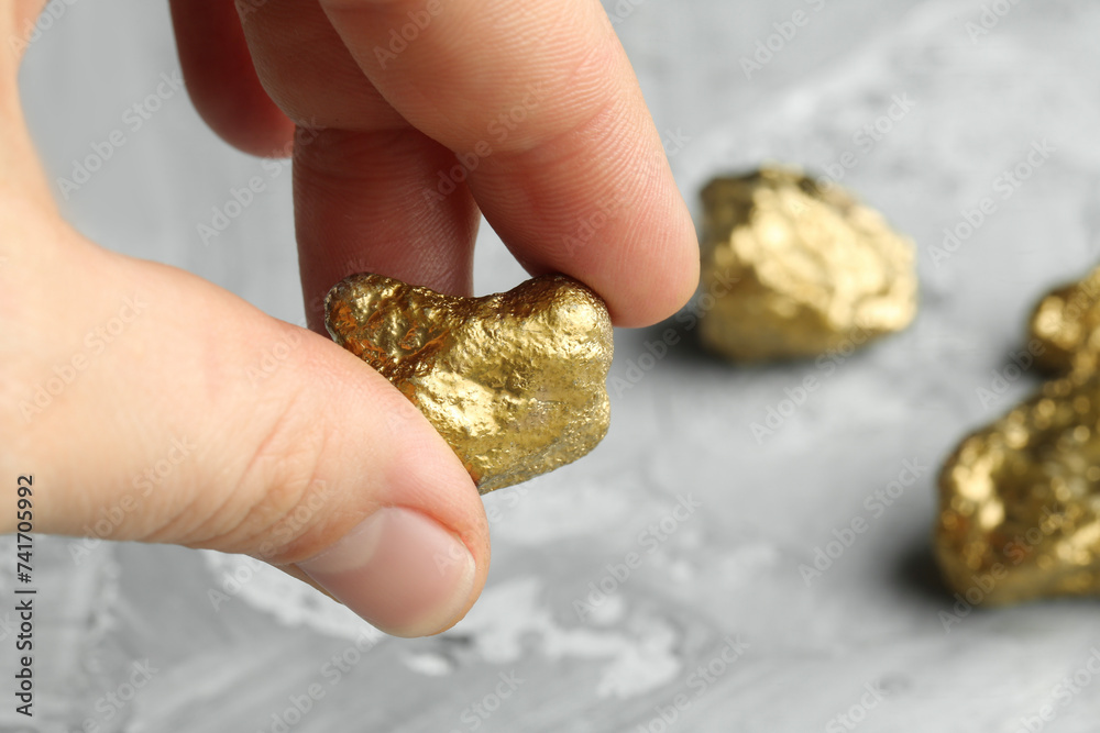 Fototapeta premium Woman holding gold nugget at grey textured table, closeup. Space for text