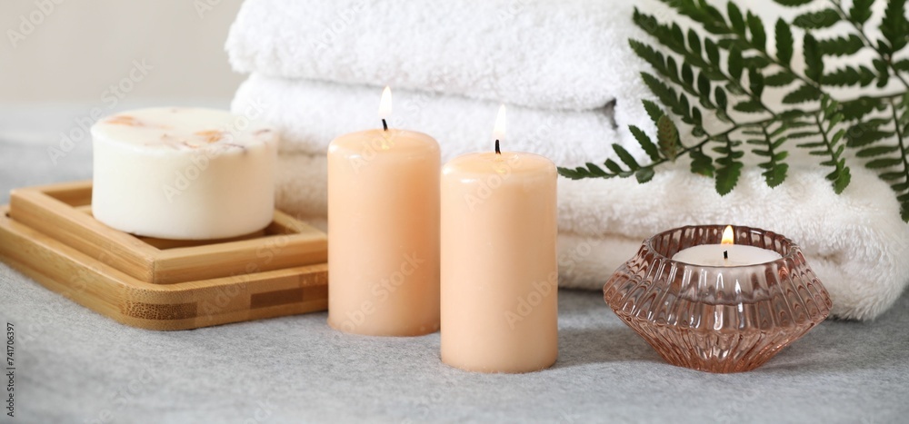 Spa composition. Burning candles, soap and towels on soft grey surface