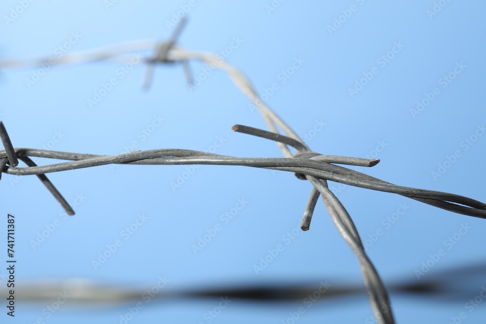 Metal barbed wire on light blue background, closeup Metal barbed wire on light blue background, closeup