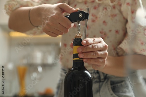 Woman opening wine bottle with corkscrew on blurred background  closeup