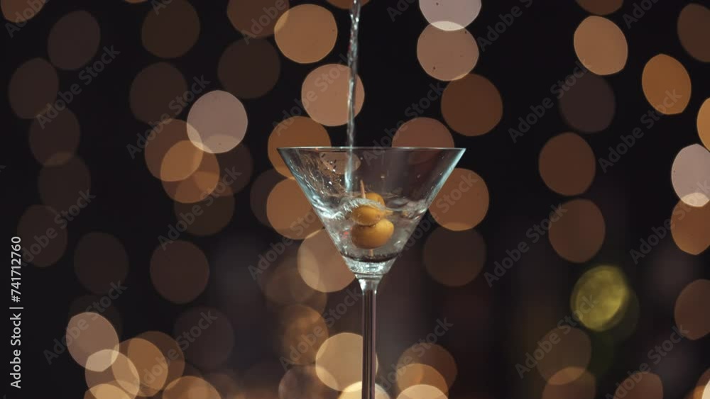 Llena la copa de Martini con alcohol líquido, tiene dos aceitunas en un palillo. Todo el fondo está desenfocado, creando un efecto bokeh con las luces de fondo. Primer plano del relleno de vidrio.