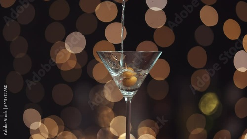 Llena la copa de Martini con alcohol líquido, tiene dos aceitunas en un palillo. Todo el fondo está desenfocado, creando un efecto bokeh con las luces de fondo. Primer plano del relleno de vidrio.