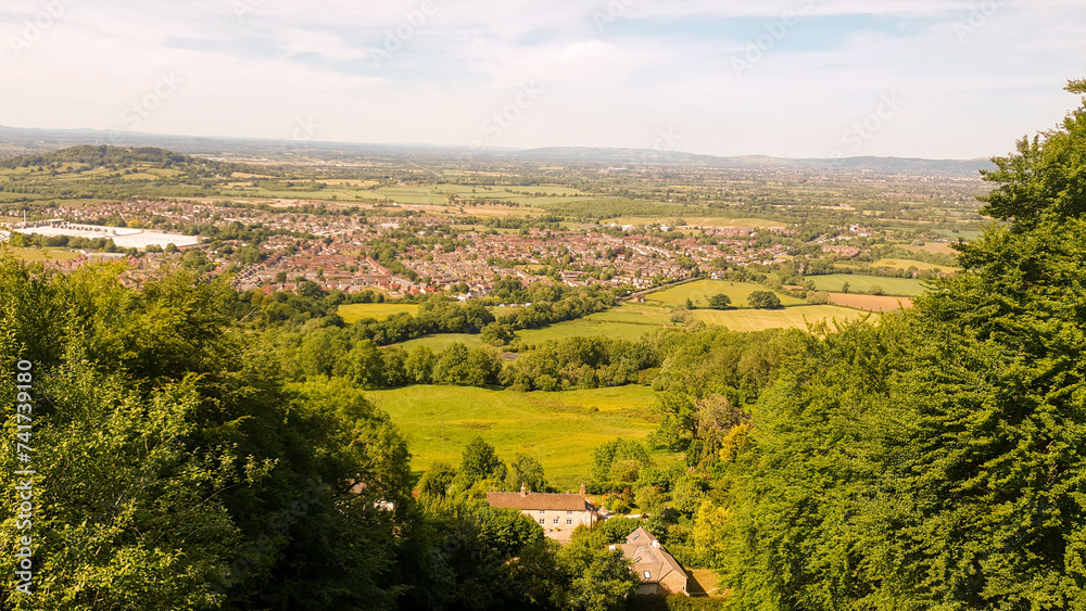 Scenic view of a lush valley with green fields, trees, and a town in the distance under a clear sky.