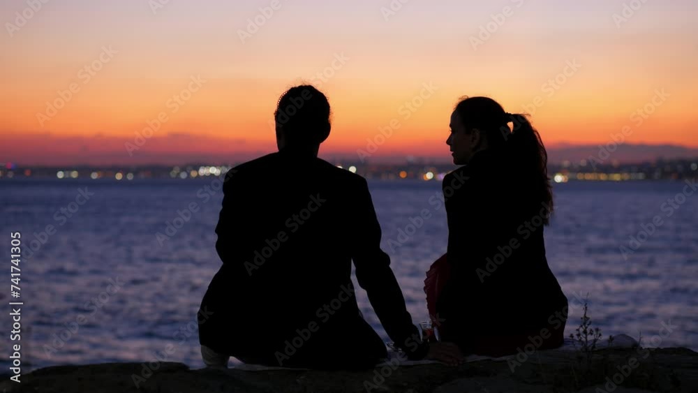 Relaxed couple sits by Istanbul waterfront in evening after sunset, admiring skyline and beautiful evening sky. They are in romantic atmosphere, enjoying peaceful ambiance of harbor. Relaxed couple sits by Istanbul waterfront in evening after sunset, admiring skyline and beautiful evening sky. They are in romantic atmosphere, enjoying peaceful ambiance of harbor.